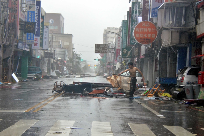 A man is holding onto debris in front of a row of shop fronts.