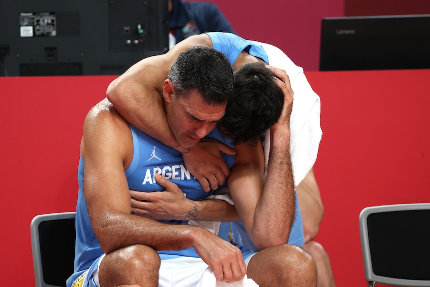 A man wearing a blue singlet is hugged by another man wearing a blue singlet