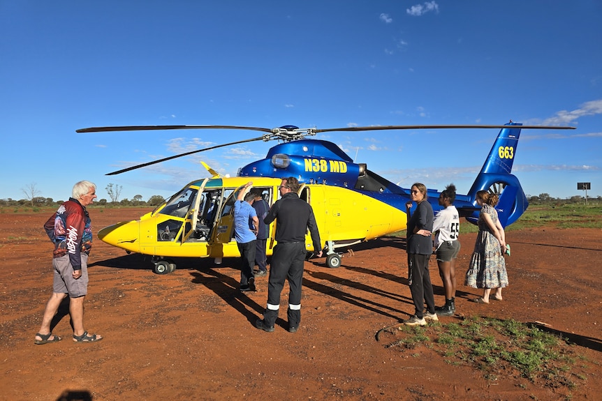People stand around a helicopter sitting in red dirt