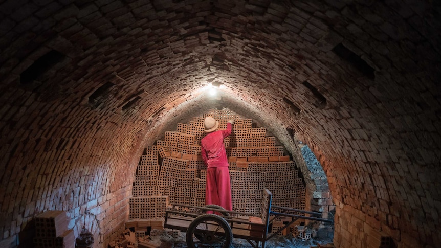 A woman removes bricks from inside a kiln in Cambodia.