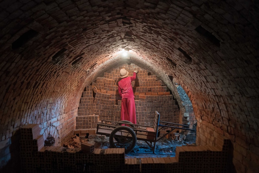 A woman removes bricks from inside a kiln in Cambodia.