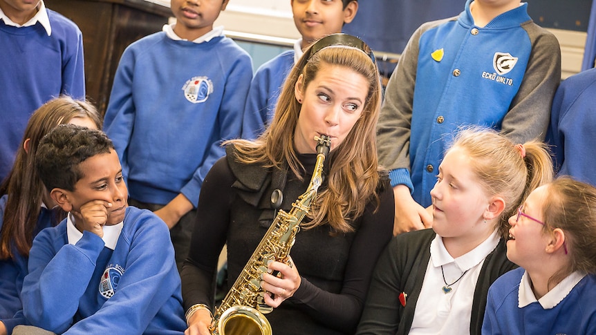 Amy Dickson performs the saxophone surrounded by schoolchildren.
