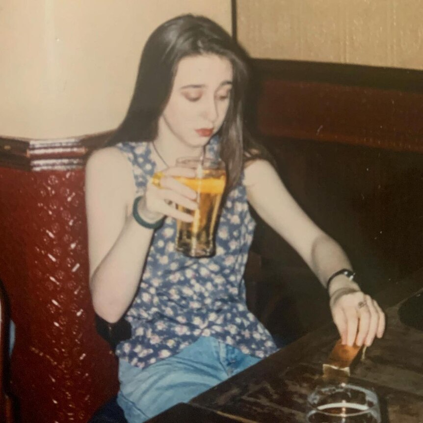 A young woman with long, dark hair holds a pint of beer.