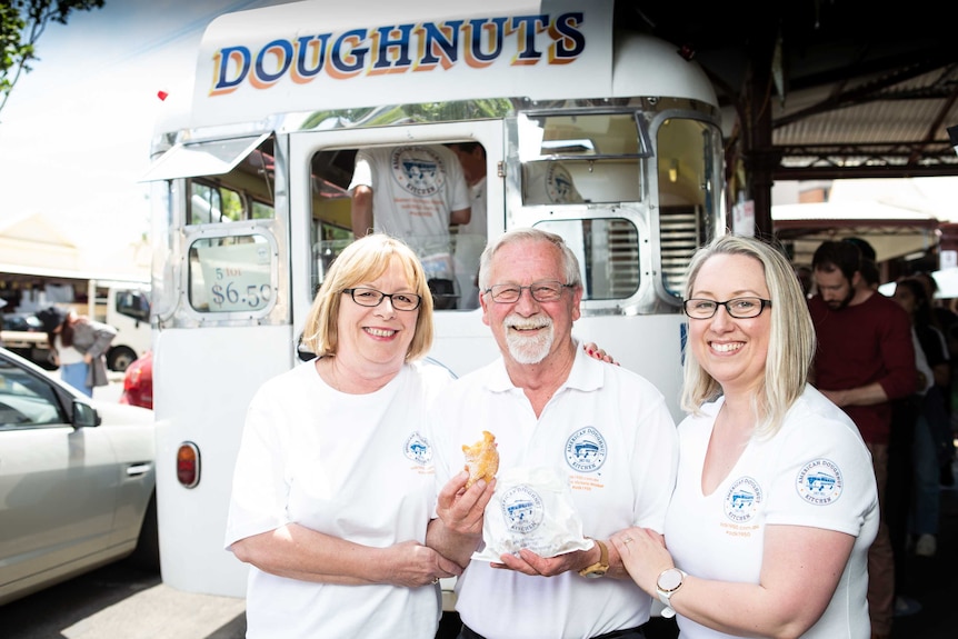 Two women and a man stand in front of a doughnut van.