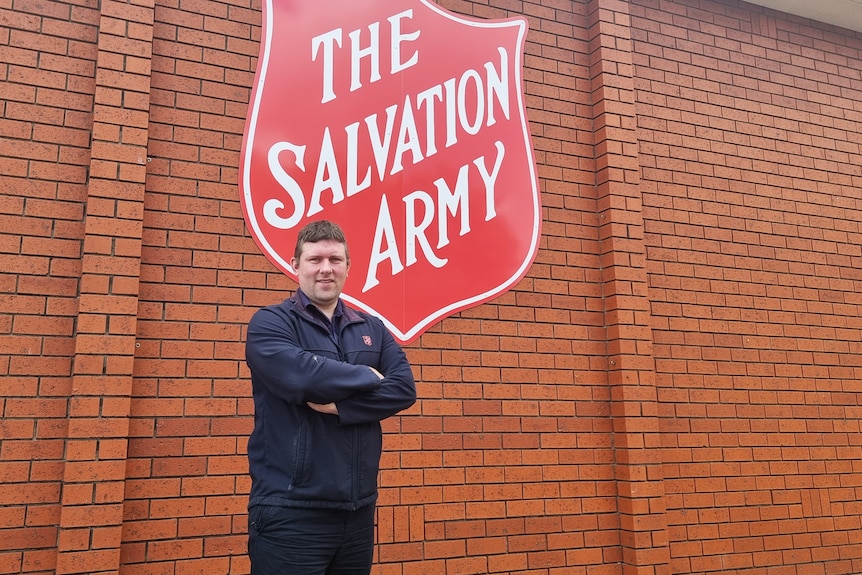 A man standing in front of a building with the Salvation Army crest.
