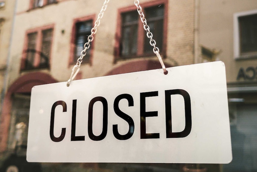 A white "closed" sign hangs on the window of a shop.