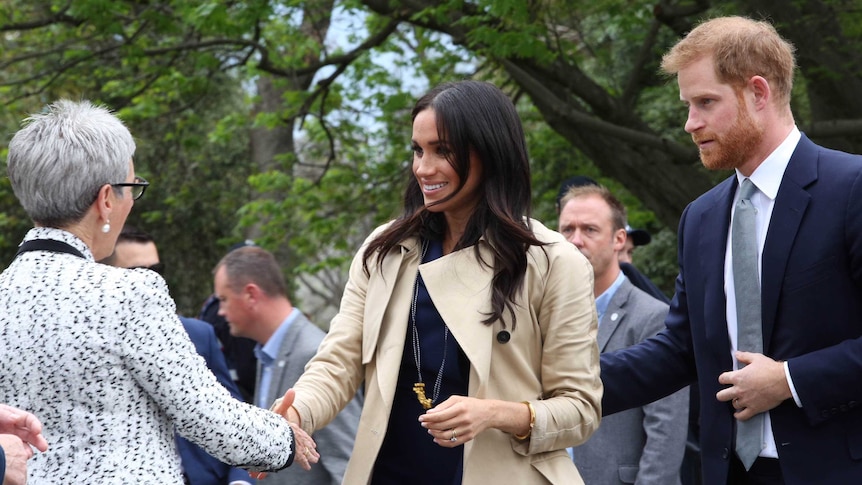 The Duchess of Sussex shakes hands with Governor Linda Dessau with Prince Harry behind her.