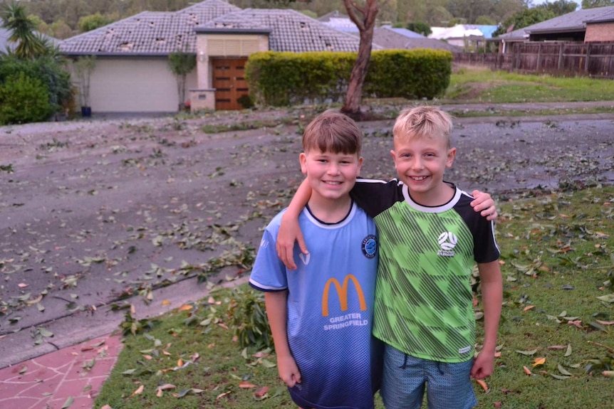 Two boys put their arms around each other with storm debris behind them.