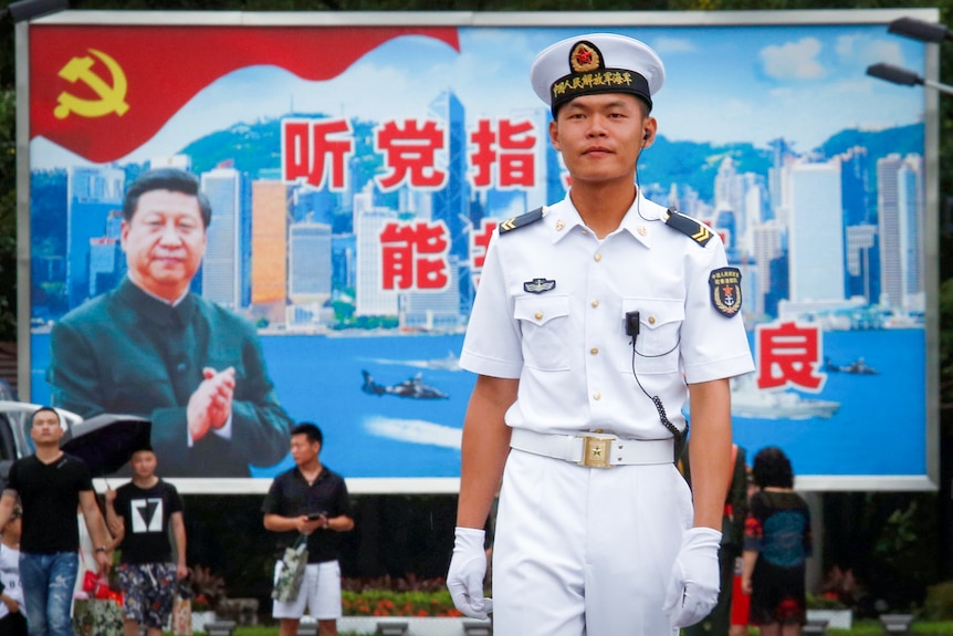 A Chinese sailor in dress white walks near a sign with Xi Jinping's face on it 