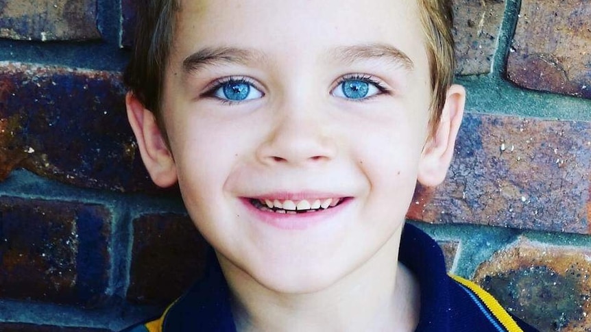 A boy about six years old with bright blue eyes smiling.
