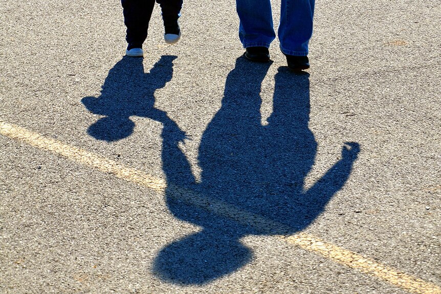 The shadows, on concrete, of a child and adult holding hands.