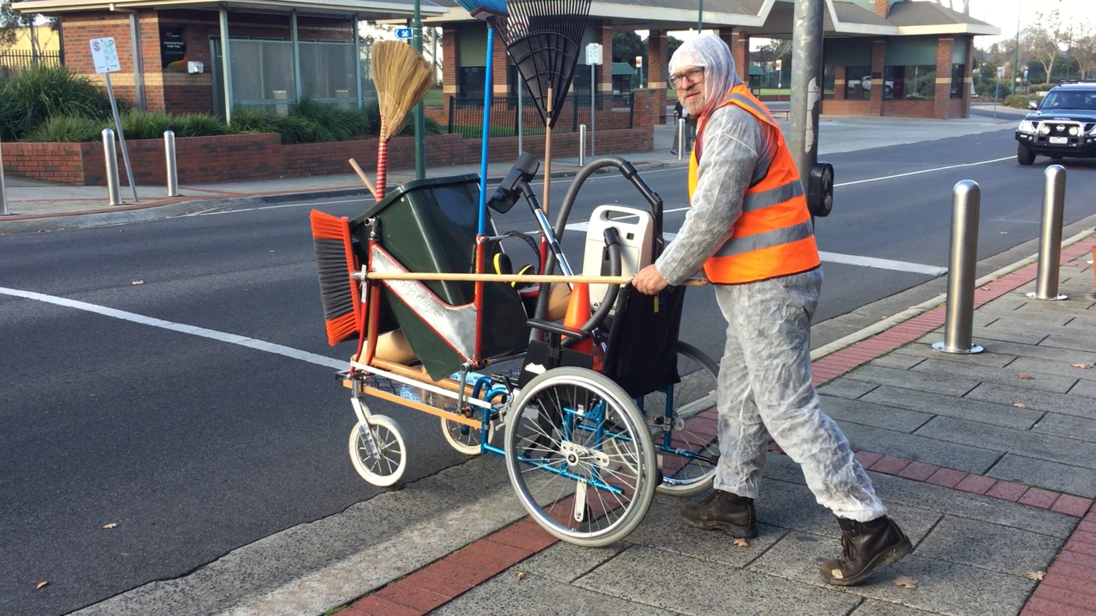 A man in his 50s with glasses and wearing protective clothing pushes a trolley filled with cleaning equipment