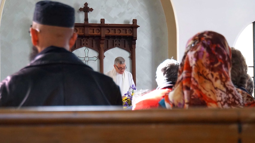 People sitting in a church listening to a priest delivering a sermon.