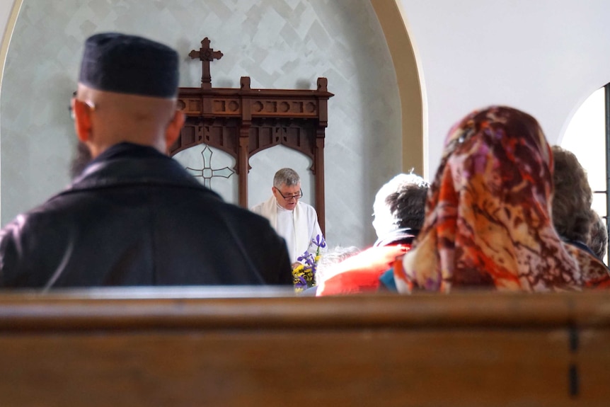 People sitting in a church listening to a priest delivering a sermon.