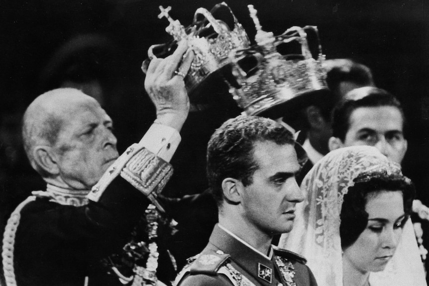 A black and white image of crowns being placed on a man and woman's heads 