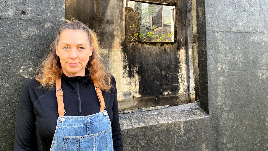 A woman in her 50s with honey coloured hair stands in front of an old ruin. 