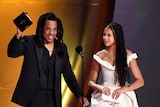 Jay-Z stands next to his daughter on stage as he holds up an award.