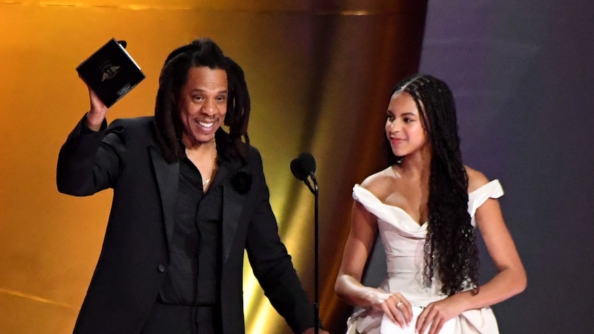 Jay-Z stands next to his daughter on stage as he holds up an award.