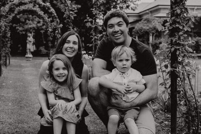 Black-and-white photo of a family consisting of a mother, father and two young kids, posing in a garden.