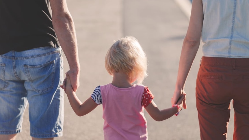 Child holds hands of mum and dad.