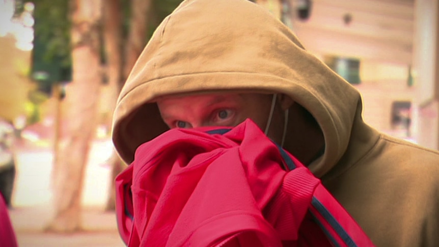 A man in a beige hoodie hiding his face with a pink jumper