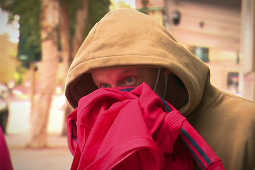 A man in a beige hoodie hiding his face with a pink jumper
