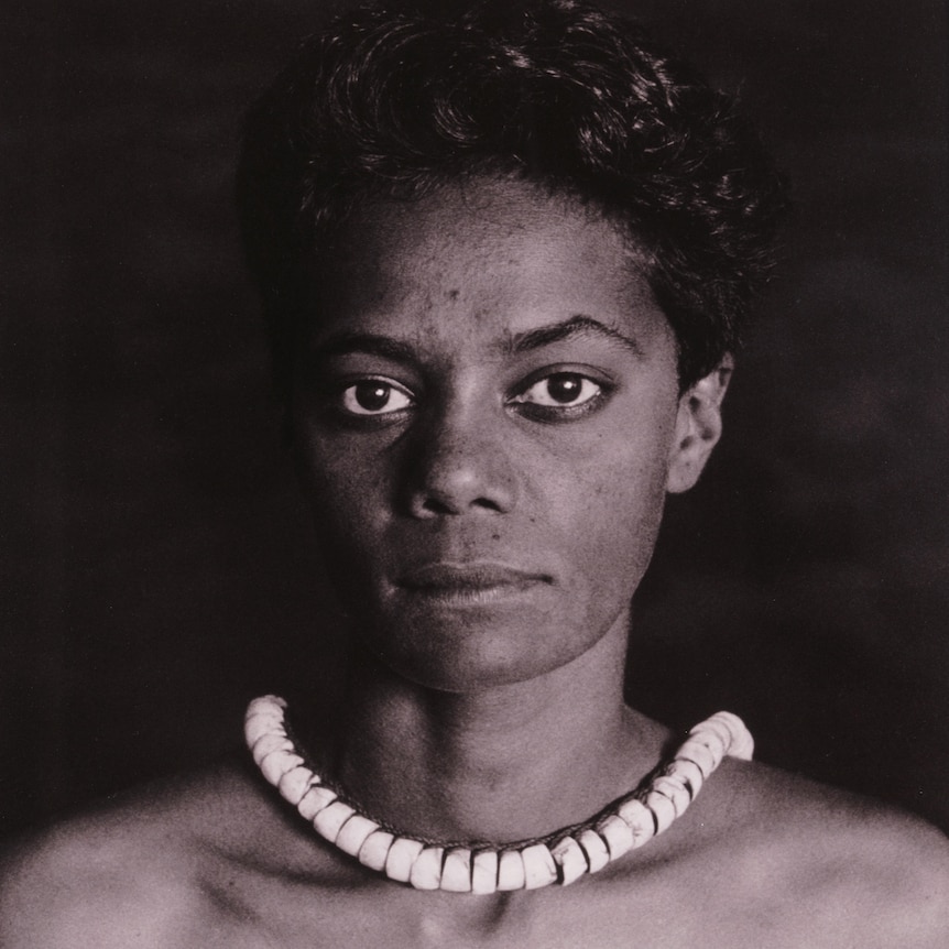 Black and white photo of a woman, hair up, wearing a white shell necklace.