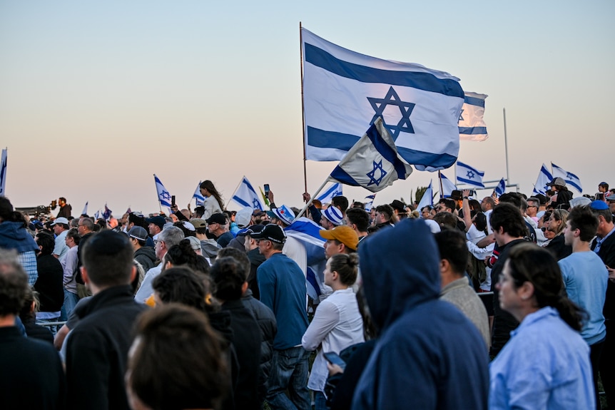 Crowd with Israeli flags at Sydney vigil, sun setting in the background