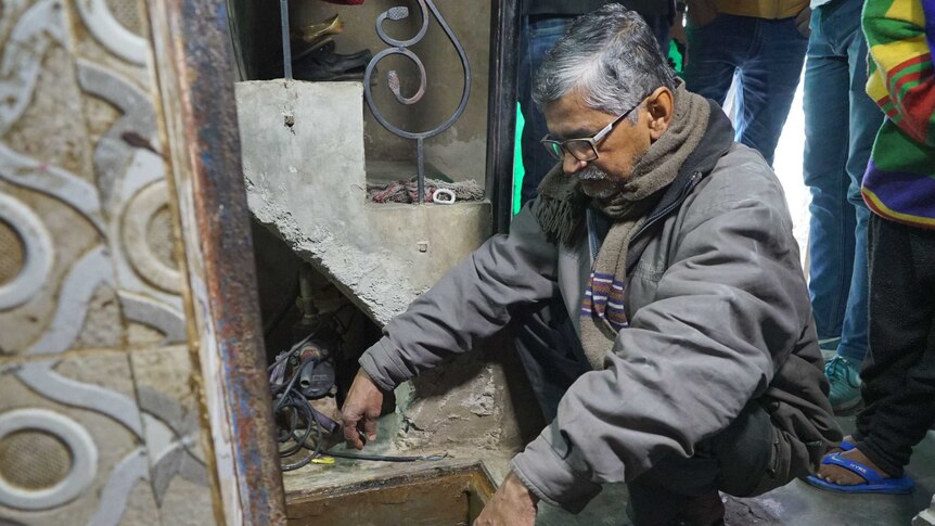 A man stares down at a hold in the floor in his house.