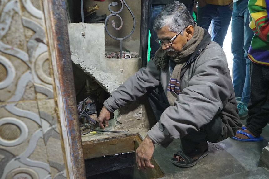 A man stares down at a hold in the floor in his house.