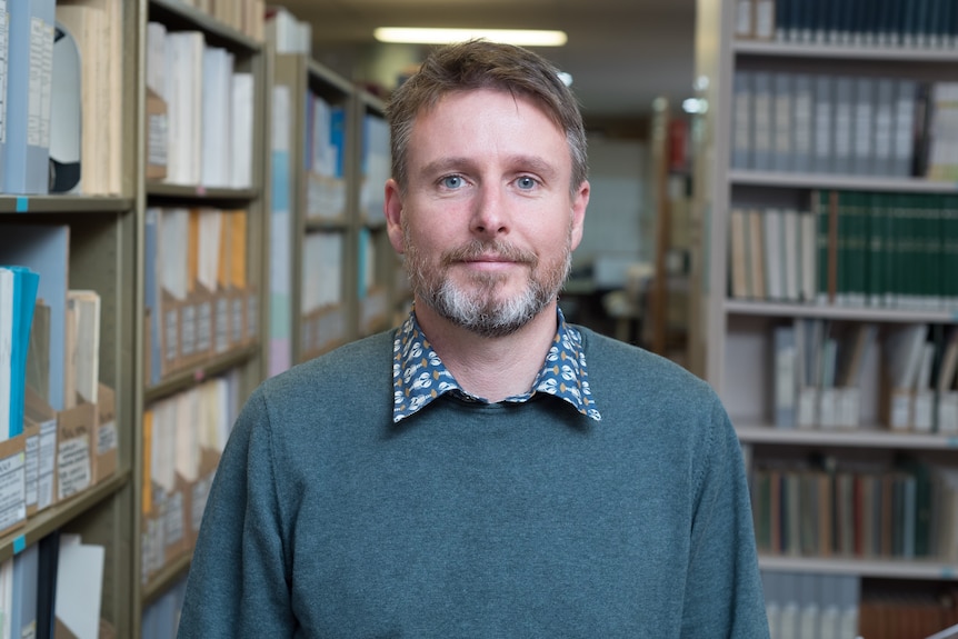 Portrait shot of a man with a short beard and brown hair wearing a jumper with a collared shirt underneath