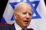 Joe Biden sits in front of Israeli and American flags. He is speaking.