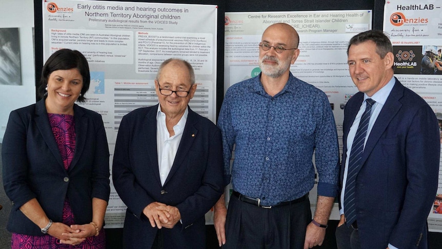 The four stand in front of posters detailing the otitis media research