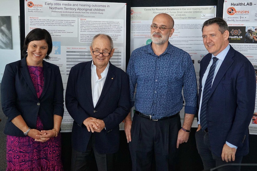 The four stand in front of posters detailing the otitis media research