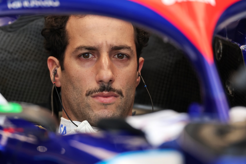 F1 driver Daniel Ricciardo, sitting in his car, in the garage, with a stern look