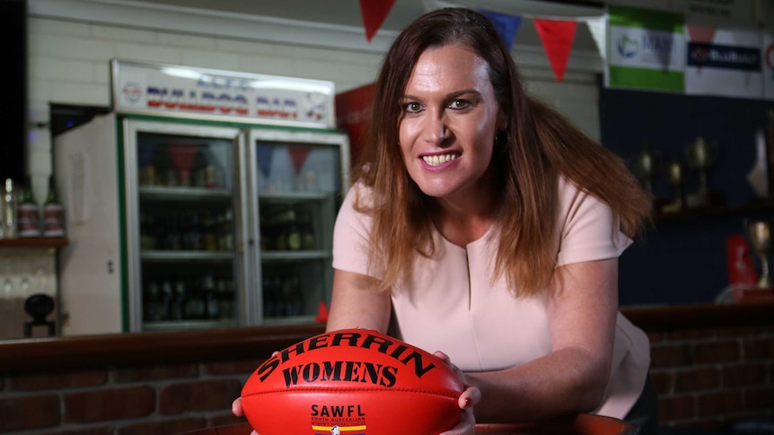 Lucy Finlay leans on a bench holding a football in her hands