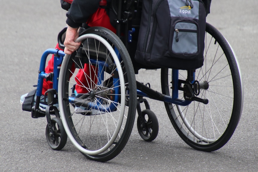 A photo of a person from heads down in a black wheelchair in an empty car park.