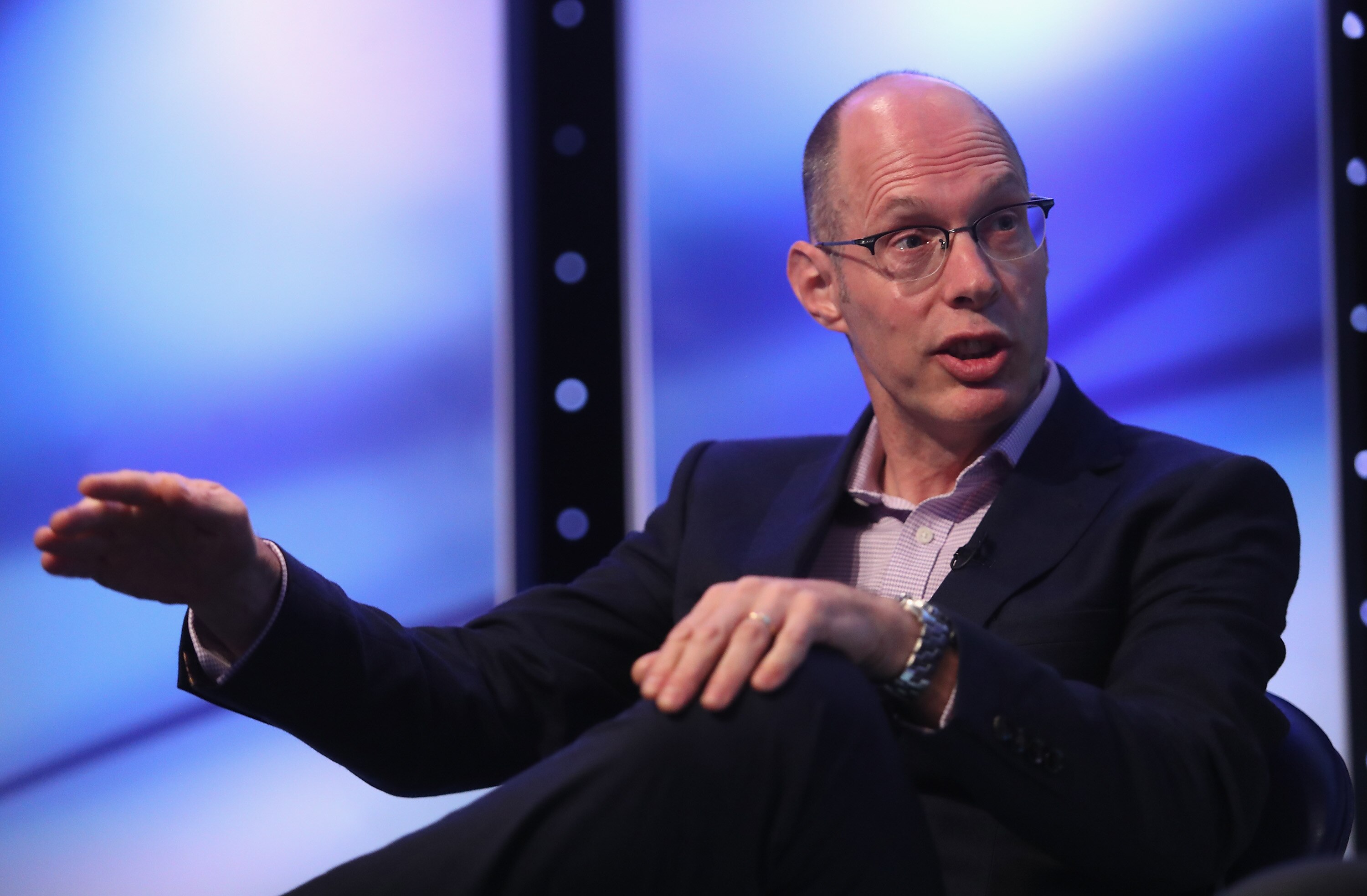 A man in a suit and glasses speaks on stage