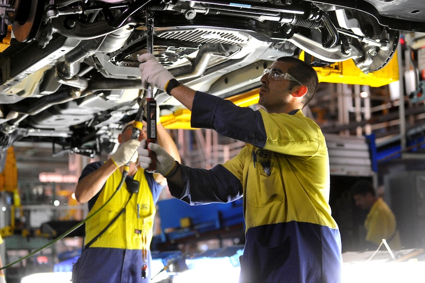 Workers underneath a car on a production line.