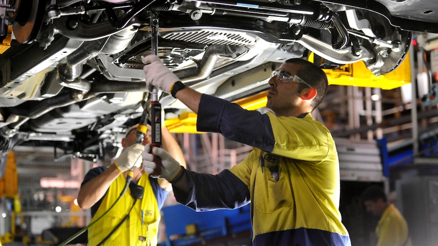 Two men work on a car at a manufacturing plant.