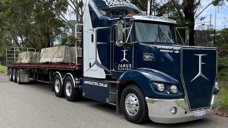 A blue and silver prime mover with a trailer attached carrying a load of cement barriers.