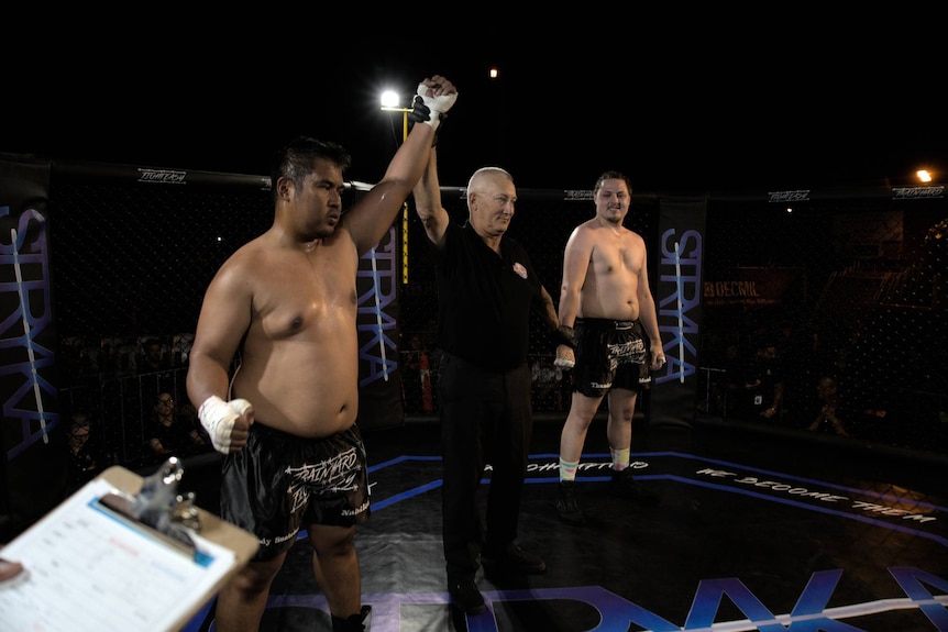 The referee raises a fighter's arm in the ring as the winner