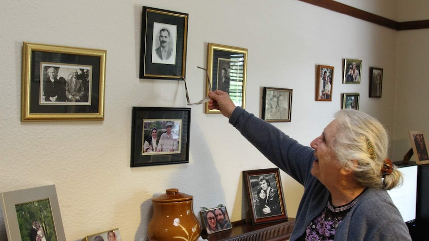 Kali Paxinos points with her glasses to one framed photo among many on the wall of her home.