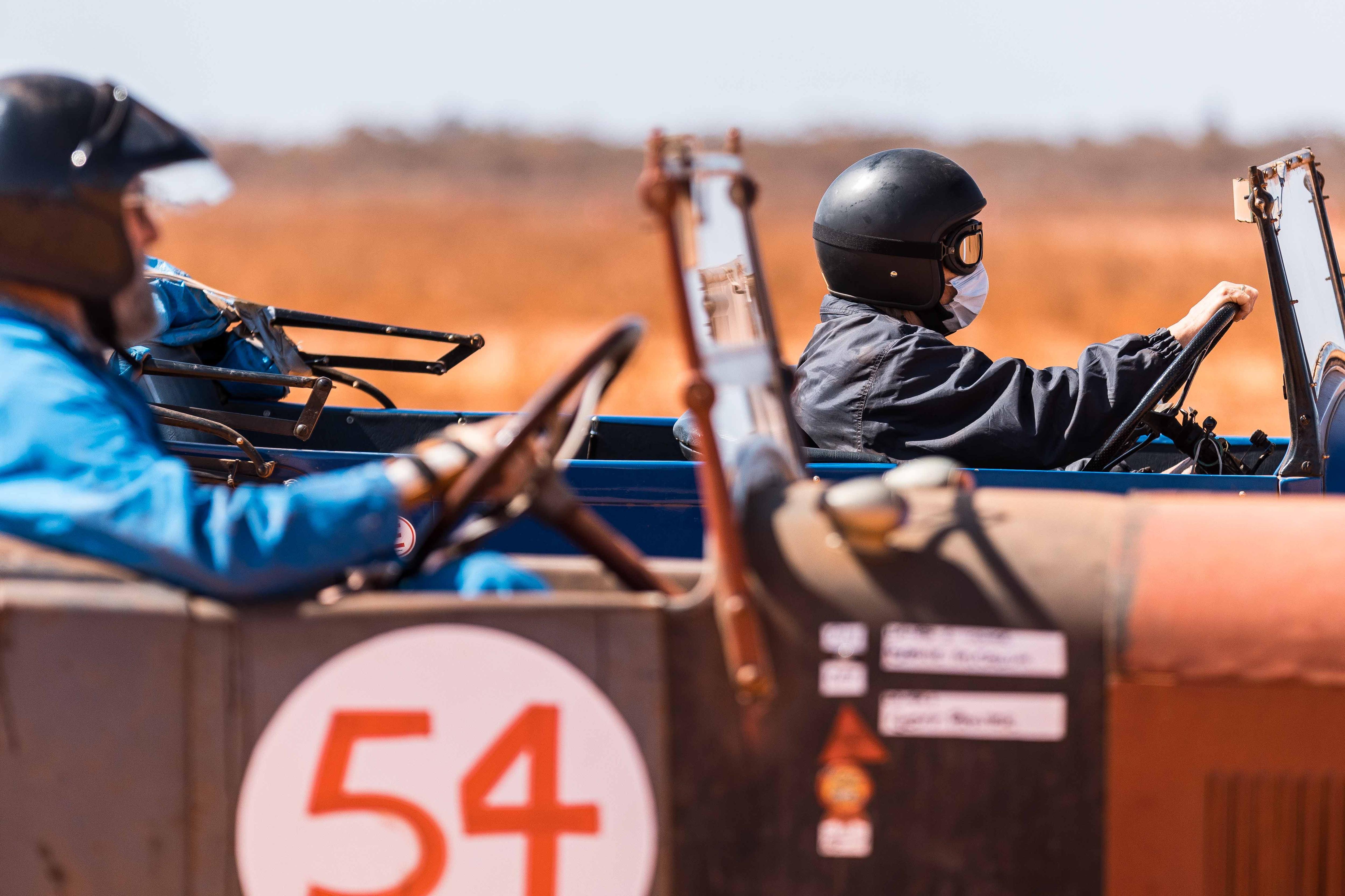 Two vintage race cars and drivers side-by-side at starting line.  