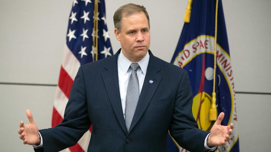 Jim Bridenstine, standing in front of US and NASA flags, gestures with his hands.