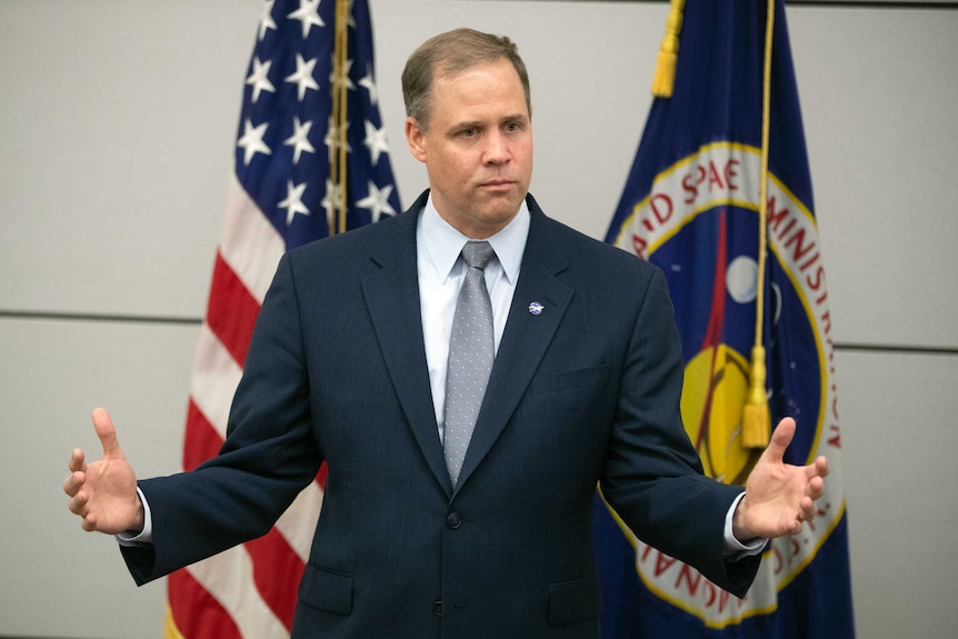 Jim Bridenstine, standing in front of US and NASA flags, gestures with his hands.