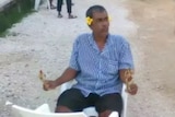 Salim Kyawning sits with yellow flowers behind his ears and small bunches in his hands.