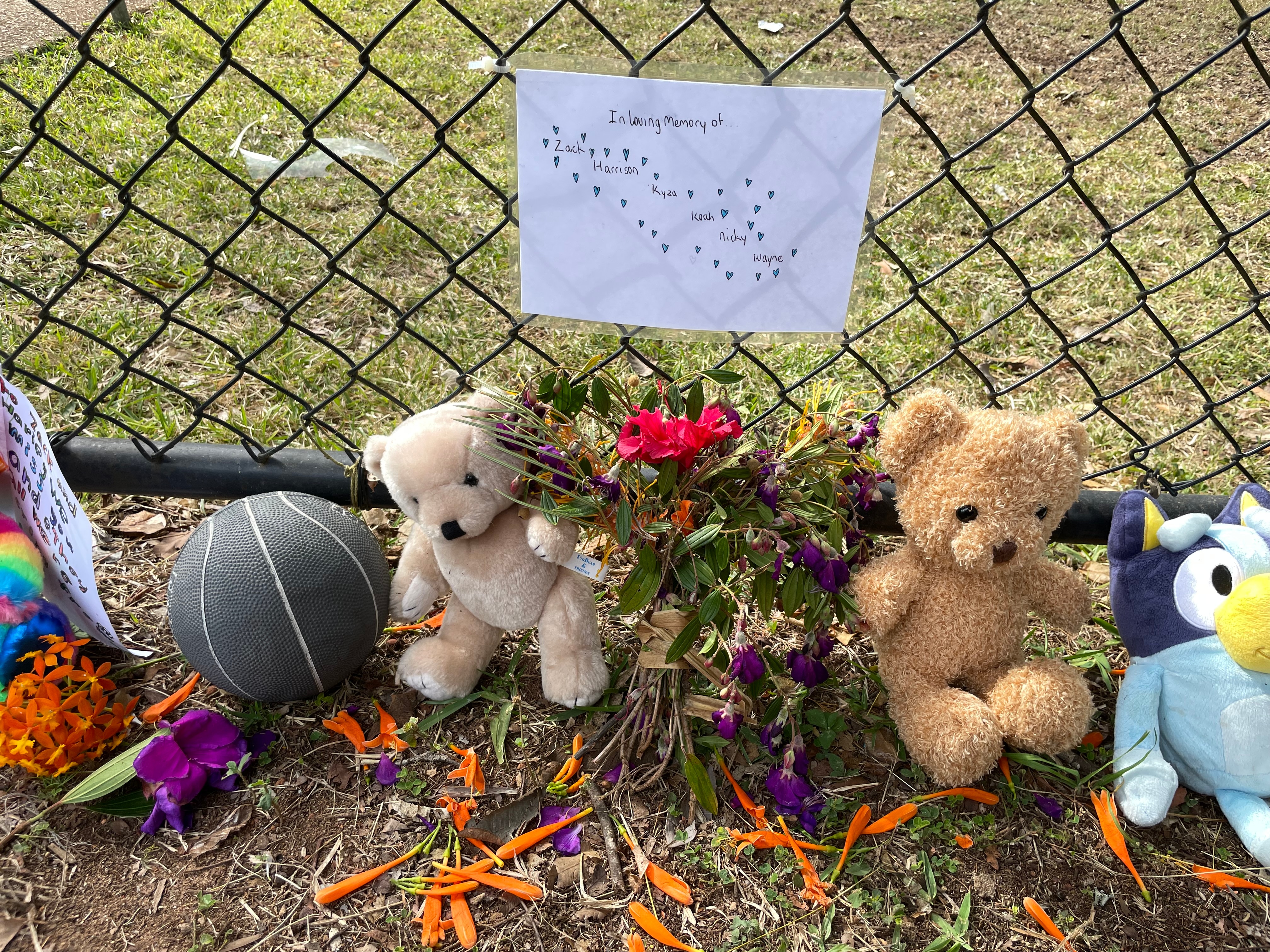 Memorial to five boys killed in Russell Island house fire with ball, teddybears resting against fence that has a drawing on it 
