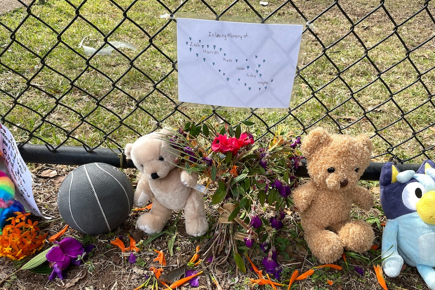 Memorial to five boys killed in Russell Island house fire with ball, teddybears resting against fence that has a drawing on it 