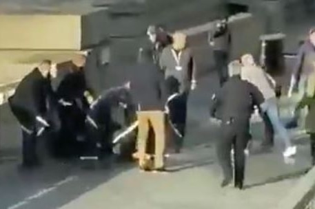 A group of men, one holding a narwhal tusk, surround a man on the ground on London Bridge.